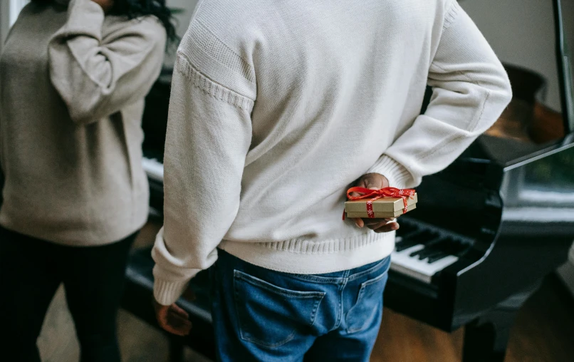 a man and a woman standing in front of a piano, pexels contest winner, holding gift, white sweater, with his back turned, gif