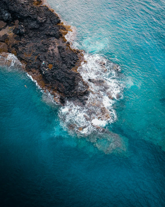 an aerial view of a large body of water, pexels contest winner, lava rock, shades of blue and grey, coming out of the ocean, near a jetty