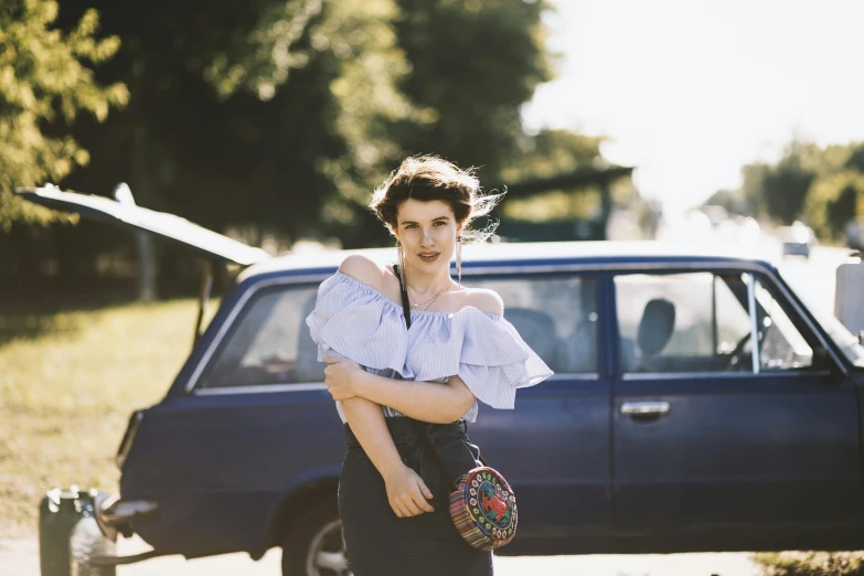 a woman standing in front of a blue car, by Lucia Peka, unsplash, renaissance, vintage clothing, portrait image, off the shoulder shirt, moskvich