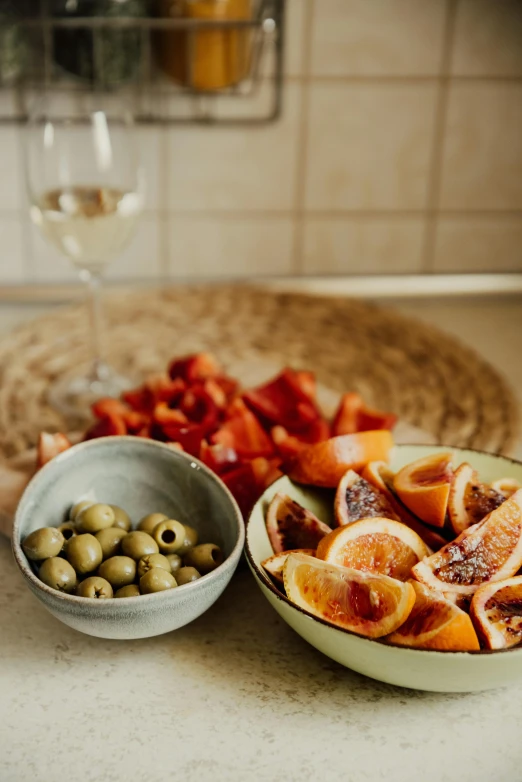 a table topped with bowls of fruit and a glass of wine, inspired by Modest Urgell, slices of orange, high quality product image”, olives, curated collection