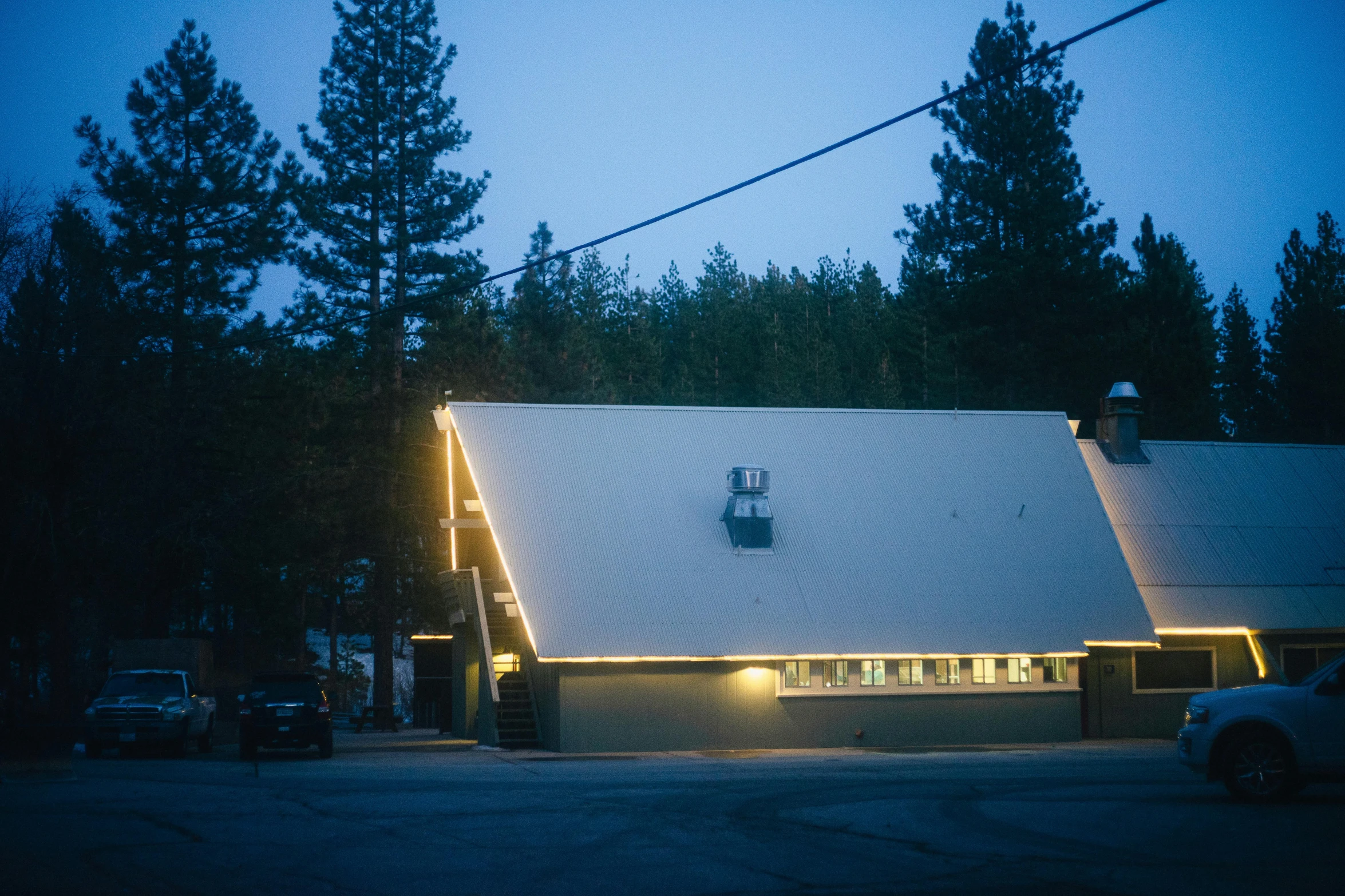a building lit up at night in a parking lot, by Ryan Pancoast, big bear lake california, roofed forest, profile image, diner
