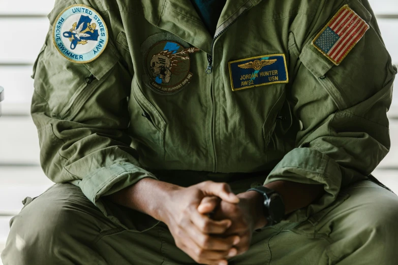 a man in a military uniform sitting on a bench, trending on unsplash, visual art, flight suit and gloves, flight squadron insignia, sitting with wrists together, embroidered uniform guard