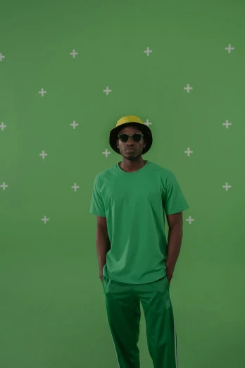 a man standing in front of a green screen, by Bascove, baggy clothing and hat, in style of tyler mitchell, chroma green background, wearing a modern yellow tshirt