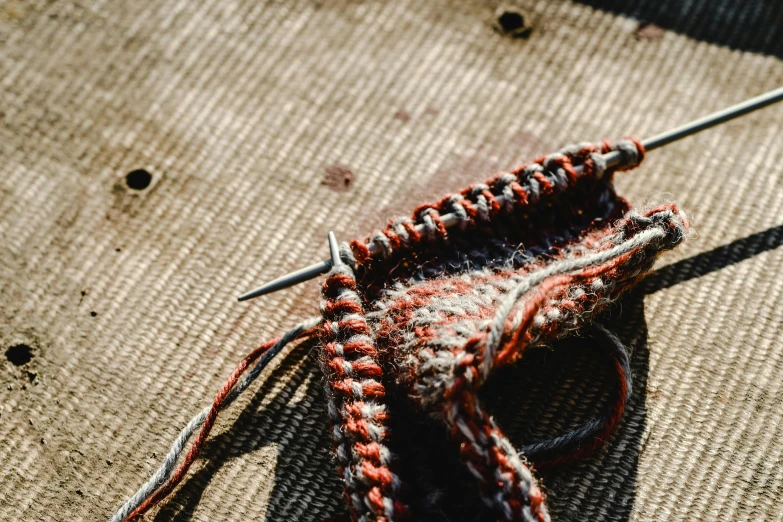 a pair of scissors sitting on top of a table, by Daniel Lieske, unsplash, process art, made of wool, red brown and grey color scheme, crochet skin, in the sun