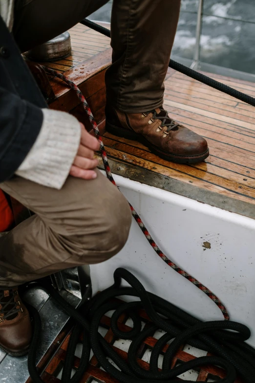 a close up of a person on a boat, leather clothing and boots, webbing, head down, wooden boat