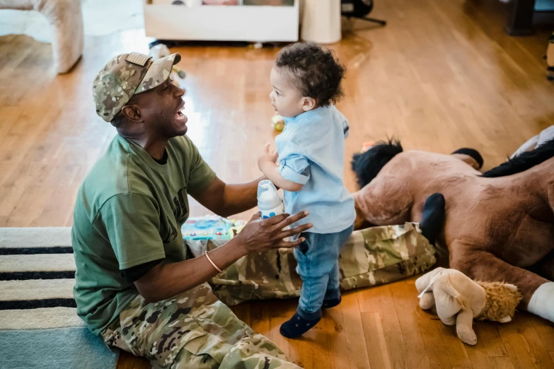 a man sitting on the floor with a baby and stuffed animals, military, african american, gen z, the horse and his boy