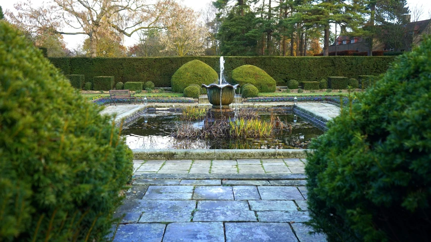 there is a fountain in the middle of a garden, inspired by Edwin Deakin, unsplash, arts and crafts movement, 2006 photograph, winter sun, verdant topiary, rule of thirds