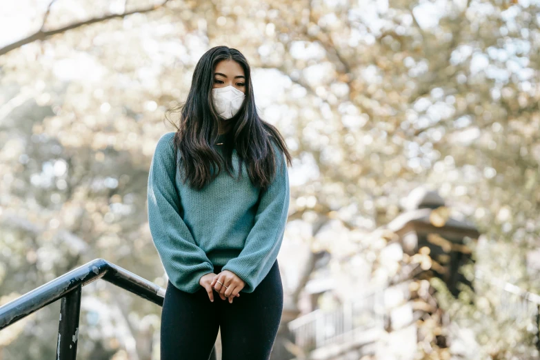 a woman wearing a face mask standing on a set of stairs, trending on pexels, sydney park, wearing sweatshirt, air pollution, gemma chan beautiful girl