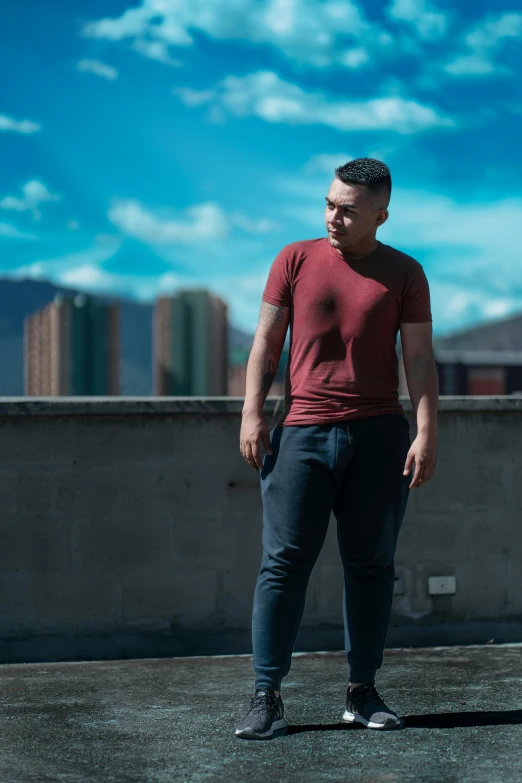 a man standing on top of a roof next to a skateboard, inspired by Eddie Mendoza, pexels contest winner, happening, red shirt brown pants, hands in pockets, profile image, peruvian looking