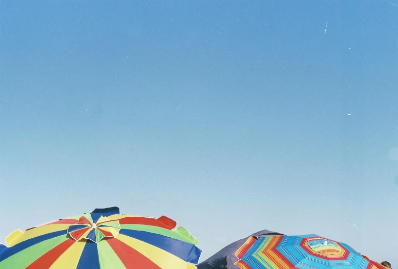 a couple of umbrellas sitting on top of a sandy beach, unsplash, minimalism, multi - coloured, low angle facing sky, awnings, martin parr