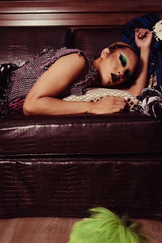 a woman laying on top of a brown couch, an album cover, inspired by Bert Stern, instagram, renaissance, wearing studded leather, green skin with scales, tessa thompson, looking exhausted