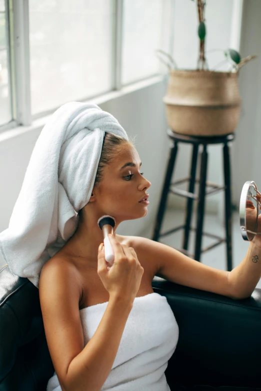 a woman sitting on a couch with a towel on her head, by Robbie Trevino, trending on pexels, renaissance, putting makeup on, dry brush, with a ponytail, reflection