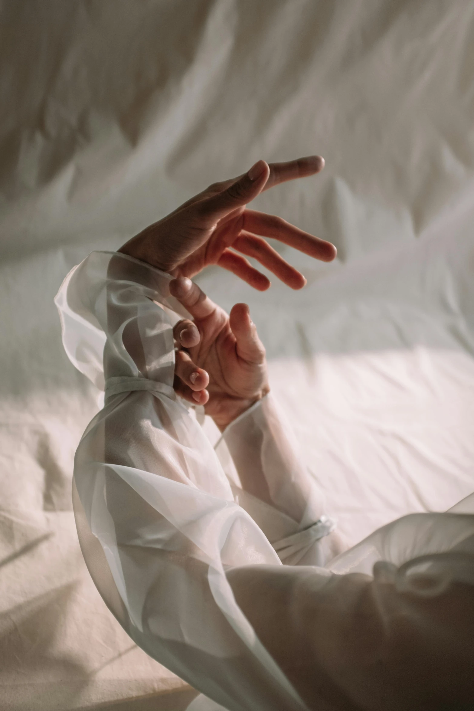 a close up of a person laying on a bed, inspired by Elsa Bleda, trending on unsplash, hyperrealism, waving robe movement, white sleeves, soft translucent fabric folds, hands shielding face