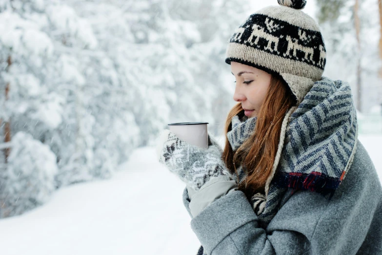 a woman standing in the snow holding a cup of coffee, inspired by Louisa Matthíasdóttir, pexels contest winner, side view intricate details, grey, drinking tea, cosy