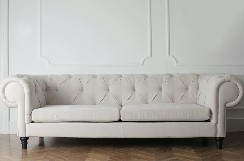 a white couch sitting on top of a hard wood floor, inspired by Constantin Hansen, pexels contest winner, arabesque, on a pale background, chesterfield, white wall, limestone