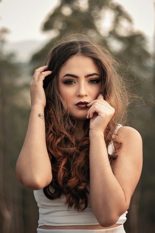 a woman in a white dress posing for a picture, inspired by Elsa Bleda, trending on pexels, brown messy hair, lipstick, weathered olive skin, hands in her hair