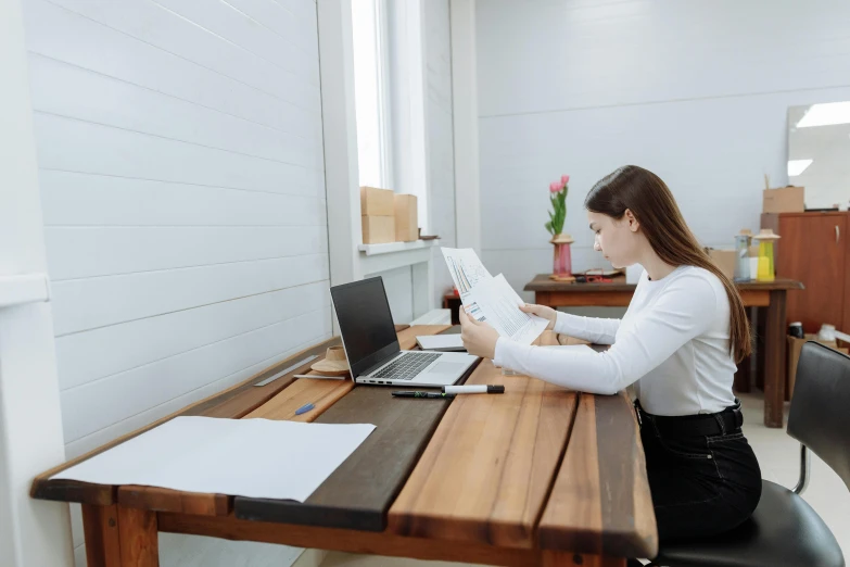 a woman sitting at a table in front of a laptop computer, pexels contest winner, academic art, sitting in an empty white room, wearing business casual dress, wooden desks with books, sydney hanson