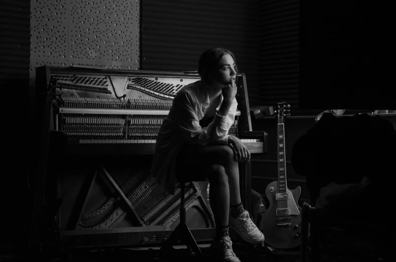 a woman sitting on a chair in front of a piano, a black and white photo, unsplash, antipodeans, jonny greenwood (lead guitar), sitting at a control center, promotional image, timothee chalamet