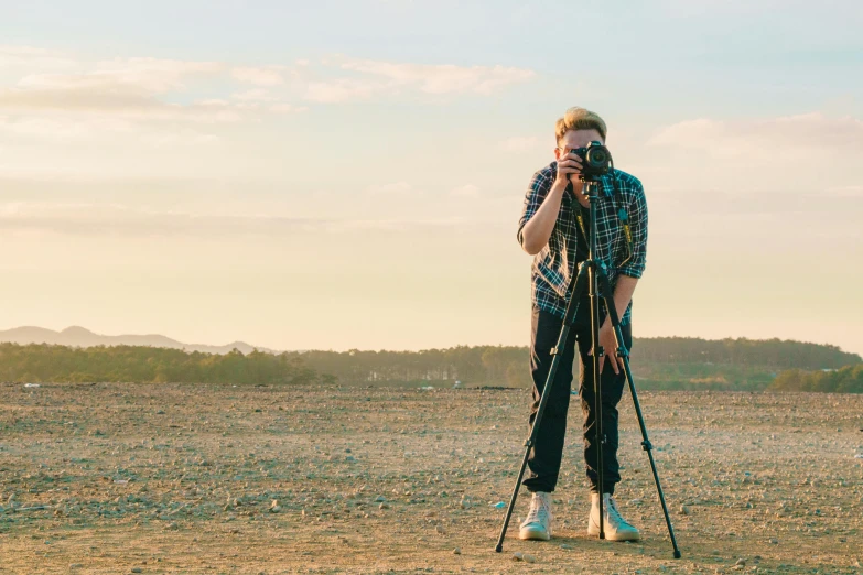 a man standing in a field holding a camera, pexels contest winner, tripod, instagram post, full body shots, long lens