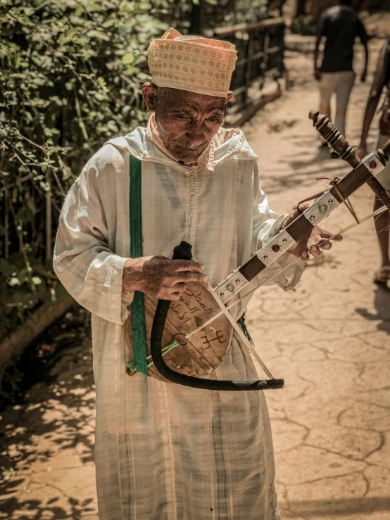 a man is playing a musical instrument on the street, an album cover, by Dan Content, pexels contest winner, happening, tuareg, wearing an elegant tribal outfit, gardening, traditional corsican