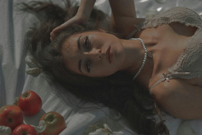 a woman laying on top of a bed next to apples, inspired by Elsa Bleda, trending on pexels, magic realism, soft devil queen madison beer, vintage footage, brooke shields, seventies cinestill