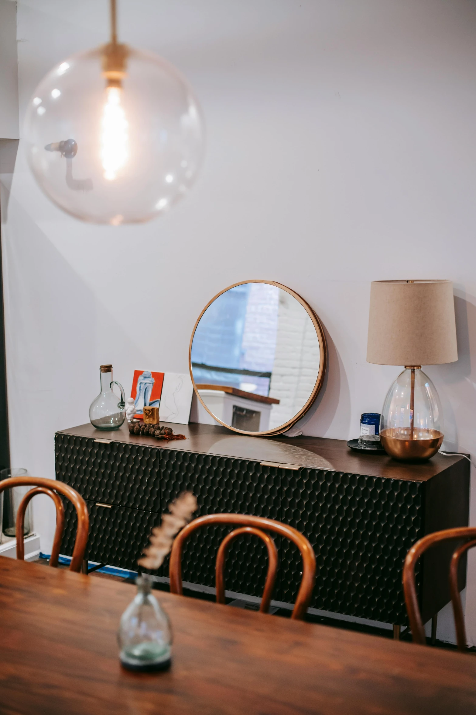 a dining room with a wooden table and chairs, pexels contest winner, light and space, round mirror on the wall, cafe lighting, profile image, hanging out with orbs