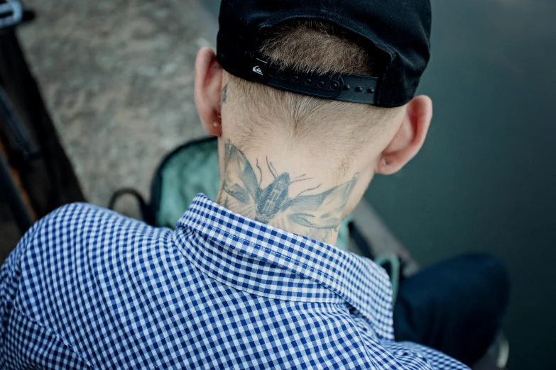 a man with a tattoo on his neck, unsplash, hyperrealism, one blue ) and huge bat ears, outdoor photo, temporary tattoo, man sitting facing away