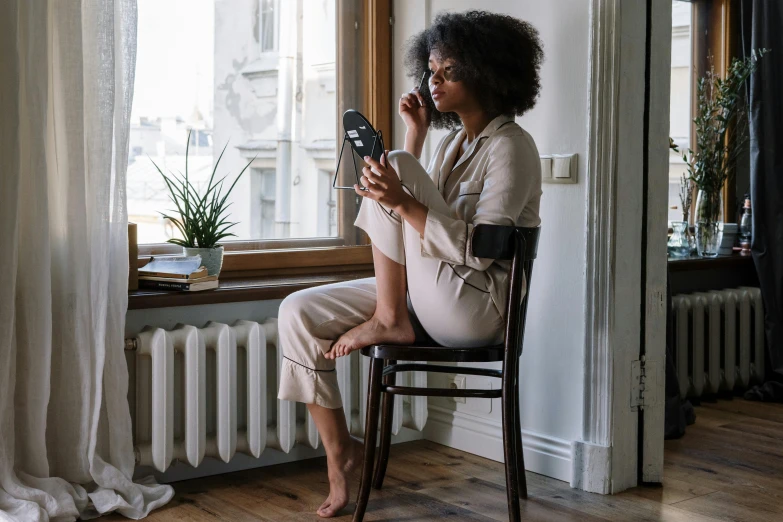 a woman sitting on a chair looking at her cell phone, by Emma Andijewska, trending on pexels, renaissance, wearing pajamas, with brown skin, with a mirror, girl making a phone call