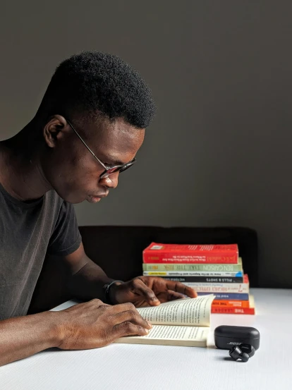 a man sitting at a table reading a book, academic art, dark-skinned, sharp focus »
