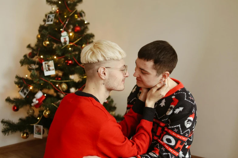 a man kissing a woman in front of a christmas tree, a photo, by Julia Pishtar, pexels, realism, two buddies sitting in a room, genderless, wearing a sweater, avatar image