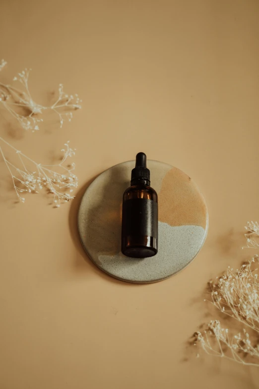 a bottle of essential oil sitting on top of a plate, by Emma Andijewska, on a large marble wall, brown resin, thumbnail, - 6