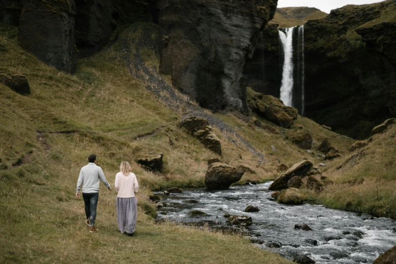 a man and a woman walking in front of a waterfall, by Hallsteinn Sigurðsson, pexels contest winner, hurufiyya, cliffs, smooth details, thumbnail, 5 5 mm photo