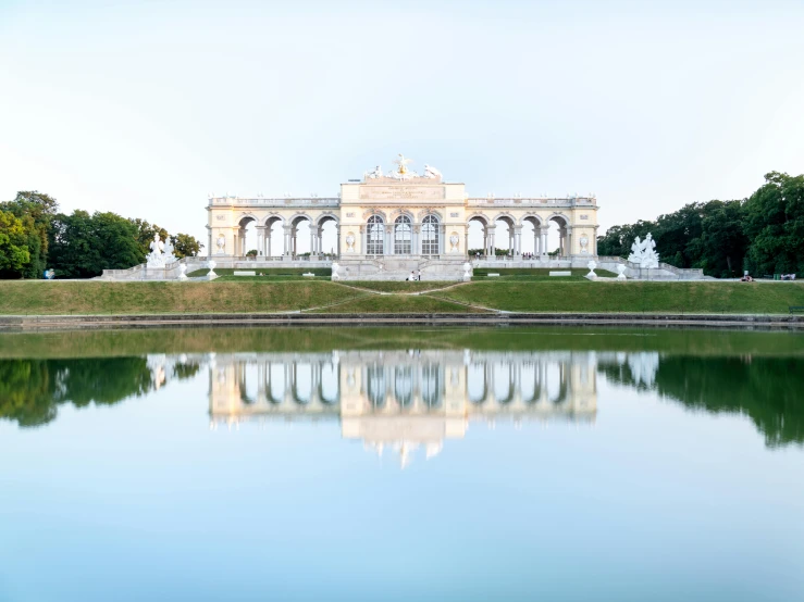 a large building sitting on top of a lush green field, a marble sculpture, by Matthias Weischer, pexels contest winner, water mirrored water, 1910s architecture, white marble buildings, sportspalast amphitheatre