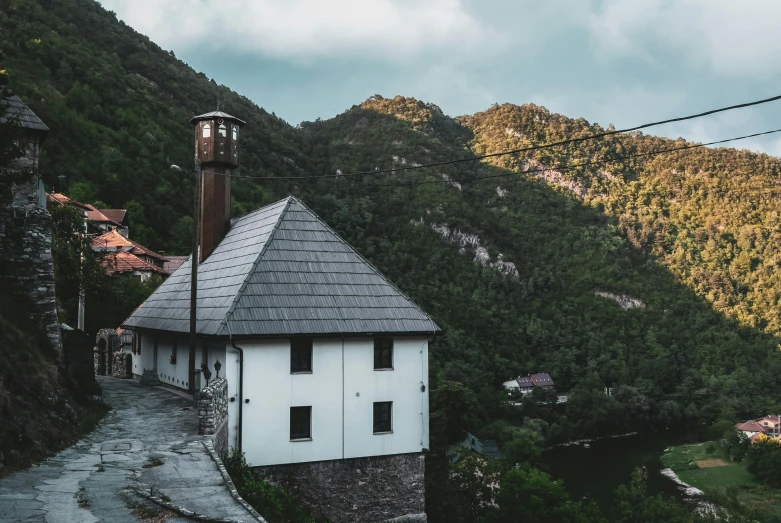 a small white building sitting on the side of a hill, by Kristian Zahrtmann, pexels contest winner, chimneys, boka, stone roof, myllypuro water tower