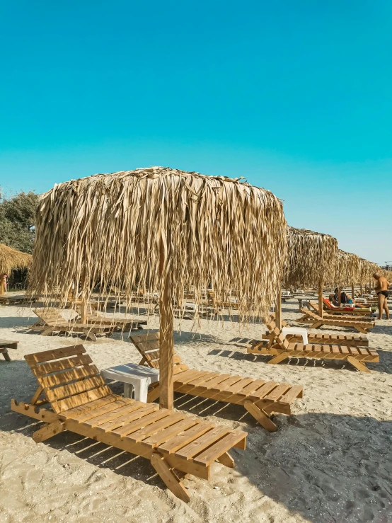 a group of lounge chairs sitting on top of a sandy beach, thatched roof, greek fantasy panorama, profile image, wooden structures