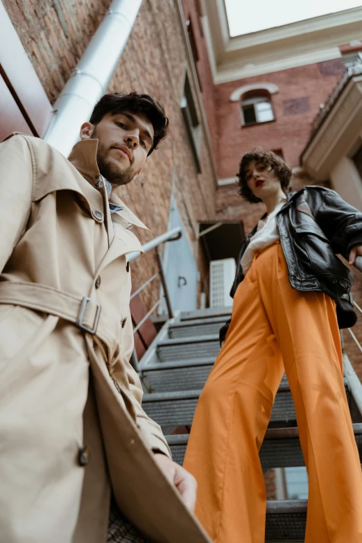 a man and a woman walking up a flight of stairs, an album cover, trending on pexels, photorealism, leather trench coat, orange jumpsuit, casual streetwear, thumbnail