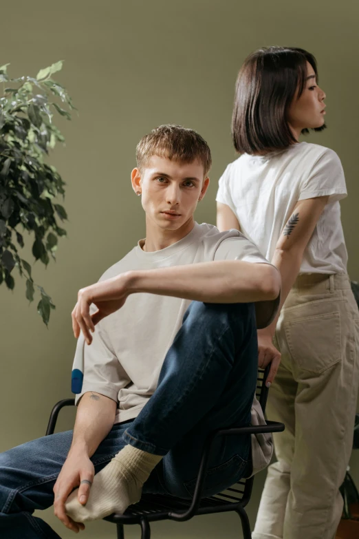 a man sitting in a chair next to a woman, trending on pexels, wearing pants and a t-shirt, non binary model, foliage clothing, ignant