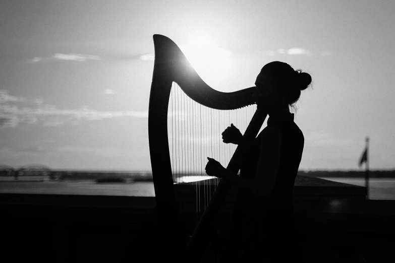 a black and white photo of a woman playing a harp, by Caroline Mytinger, pexels contest winner, romanticism, silhouette over sunset, backlit ears, instagram post, oceanside