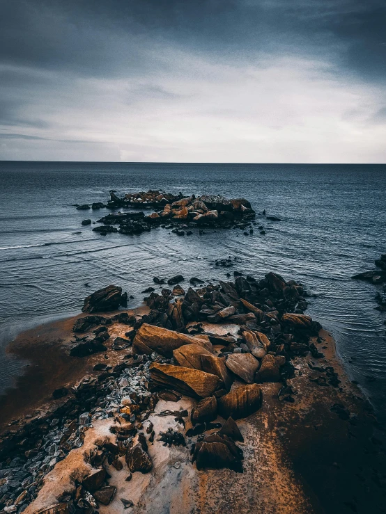 a rocky beach next to the ocean under a cloudy sky, by Jesper Knudsen, unsplash contest winner, romanticism, rich deep moody colors, today\'s featured photograph 4k, stepping stones, pov photo