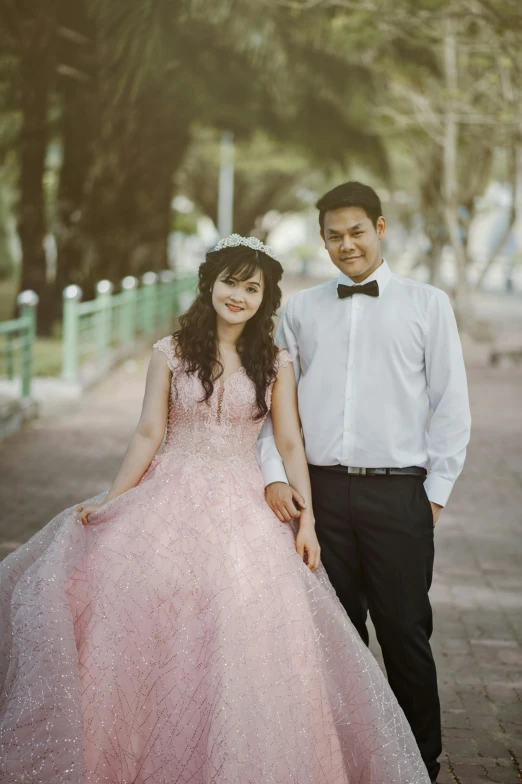 a man standing next to a woman in a pink dress, a colorized photo, by Basuki Abdullah, pexels contest winner, romanticism, wearing a formal dress, square, college, with crown