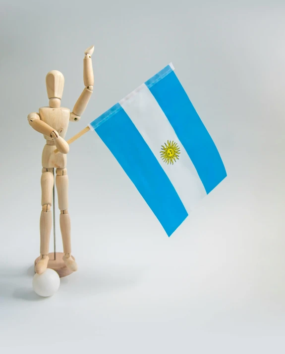 a wooden mannequin holding a argentina flag, pexels contest winner, figuration libre, arms stretched out, ilustration, miniature product photo, leg high