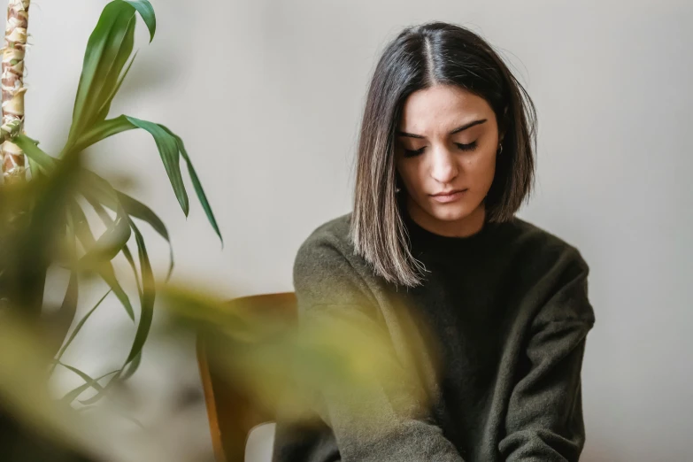 a woman sitting at a table reading a book, a portrait, by Emma Andijewska, trending on pexels, woman made of plants, brown sweater, young middle eastern woman, apprehensive mood