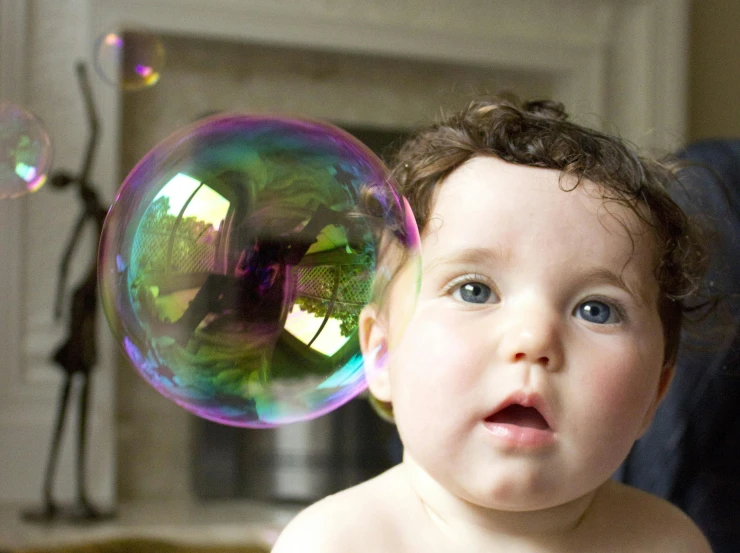 a baby is playing with soap bubbles in a living room, by Paul Davis, pexels, close - up face portrait from up, multicoloured, isaac newton, holding a balloon