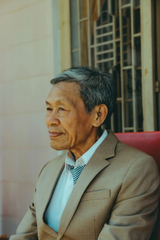 a man in a suit sitting on a red chair, inspired by Li Tiefu, pexels contest winner, sumatraism, portrait photo of an old man, profile image, myanmar, old gray hair