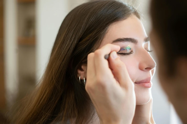 a woman putting on makeup in front of a mirror, trending on pexels, rainbow eyes, glitter gif, face painting, woman with braided brown hair