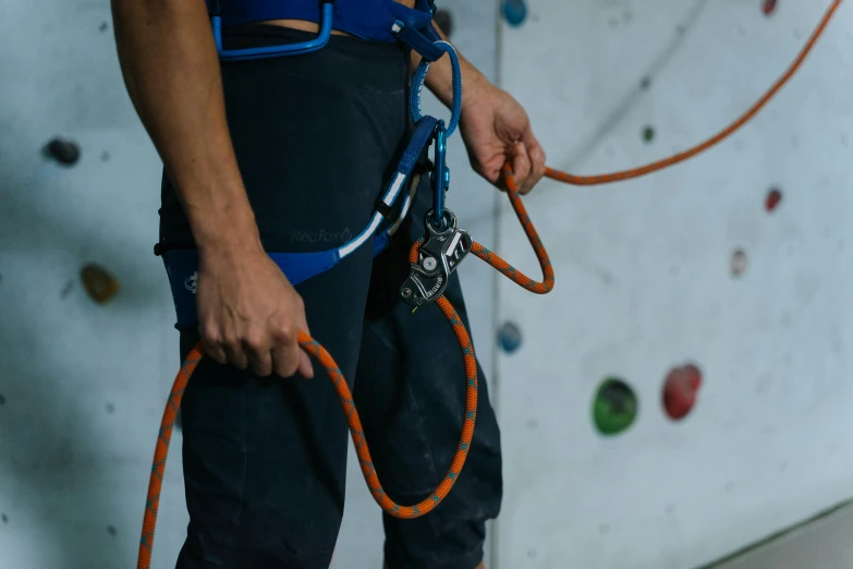 a man holding a rope while standing in front of a climbing wall, blue orange, profile image, detailing, middle shot