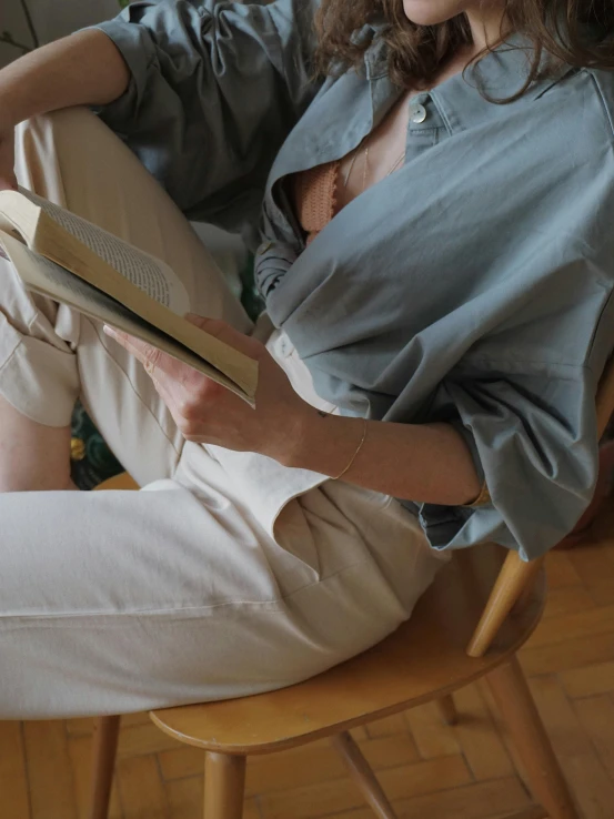 a woman sitting in a chair reading a book, by Christen Dalsgaard, wear's beige shirt, male ulzzang, cropped wide sleeve, wearing a light blue shirt