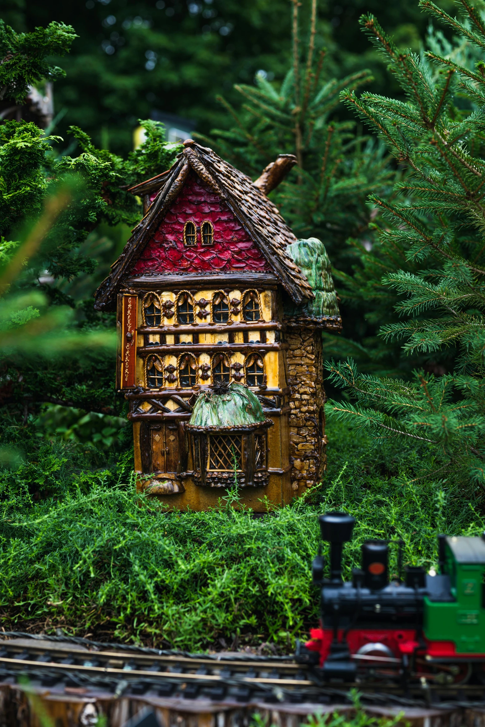 a miniature house sitting on top of a train track, inspired by Jules Tavernier, folk art, enchanting lighting, nestled in a forest, exterior shot, made of glazed