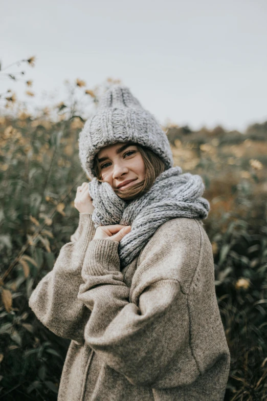 a woman standing in a field wearing a hat and scarf, trending on pexels, grey sweater, cozy environment, stubble, model wears a puffer jacket