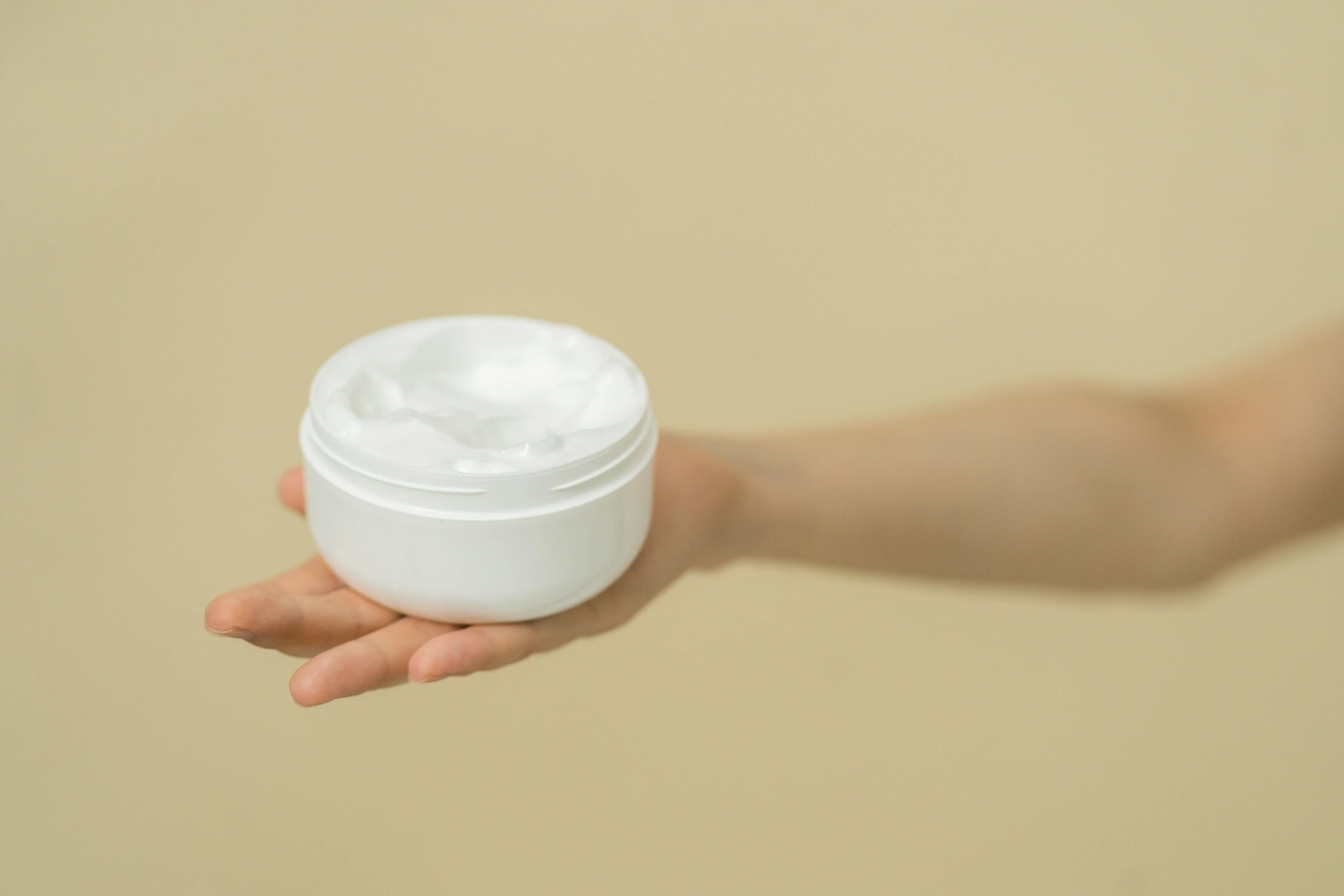 a person holding a jar of cream in their hand, detailed product image, white foam, round-cropped, fan favorite